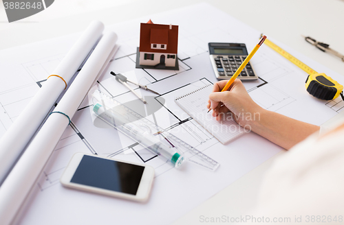 Image of close up of hand on blueprint writing to notebook