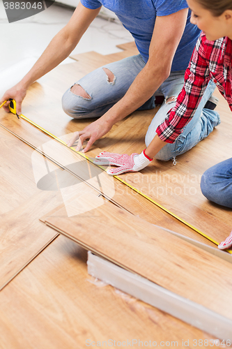 Image of happy couple with ruler measuring parquet board