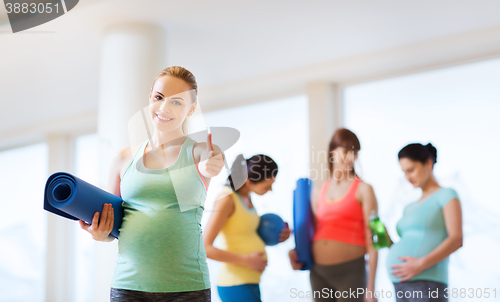 Image of pregnant woman with mat in gym showing thumbs up 