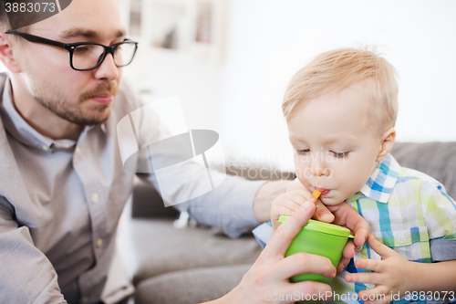 Image of father and son drinking from cup at home
