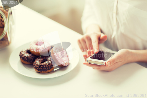 Image of close up of hands with smart phone and donuts