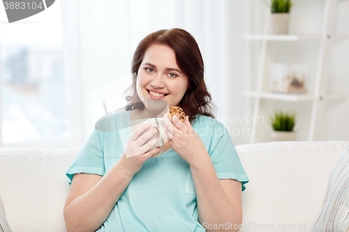 Image of happy plus size woman with cup and cookie at home