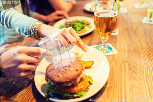 Image of close up of friends hands sharing burger at bar