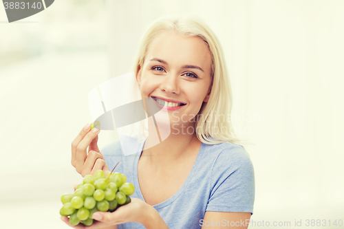 Image of happy woman eating grapes at home