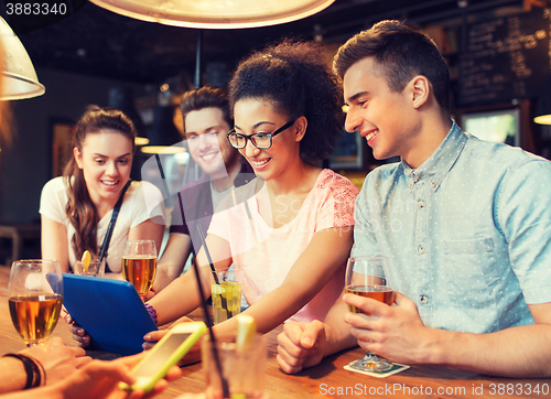Image of happy friends with tablet pc and drinks at bar