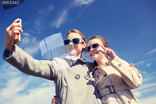 Image of happy girls with smartphone taking selfie outdoors