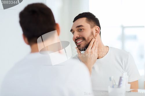 Image of happy young man looking to mirror at home bathroom