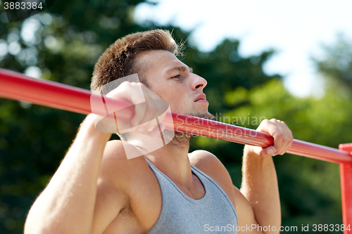 Image of young man exercising on horizontal bar outdoors