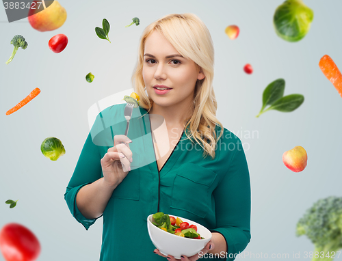 Image of smiling young woman eating vegetable salad