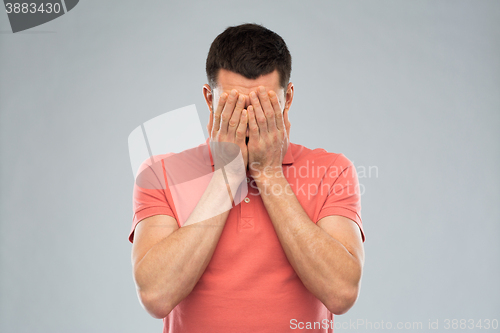 Image of man in t-shirt covering his face with hands