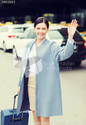 Image of smiling young woman with travel bag waving hand