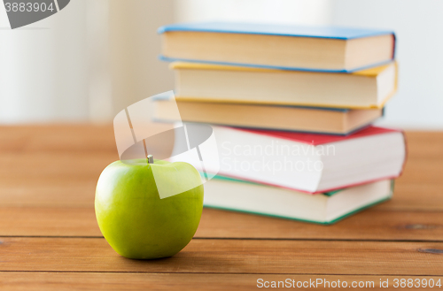 Image of close up of books and green apple on wooden table