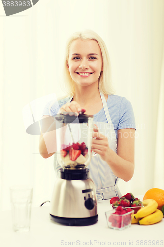 Image of smiling woman with blender preparing shake at home