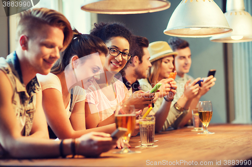 Image of happy friends with smartphones and drinks at bar