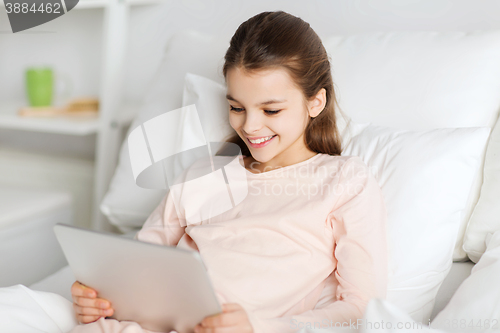 Image of happy girl lying in bed with tablet pc at home