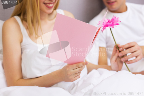 Image of close up of couple in bed with postcard and flower