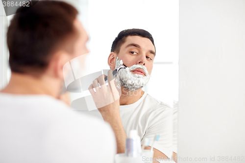 Image of man shaving beard with razor blade at bathroom