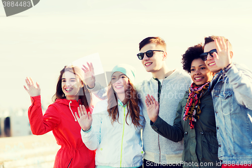 Image of happy teenage friends waving hands on city street