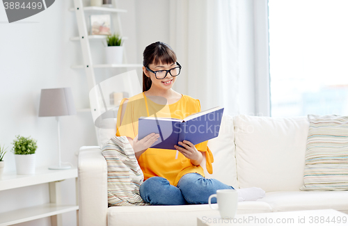 Image of smiling young asian woman reading book at home