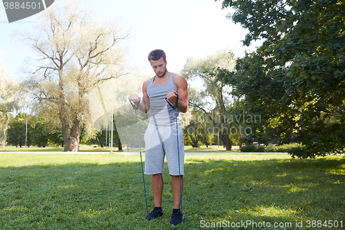 Image of young man exercising with expander in summer park