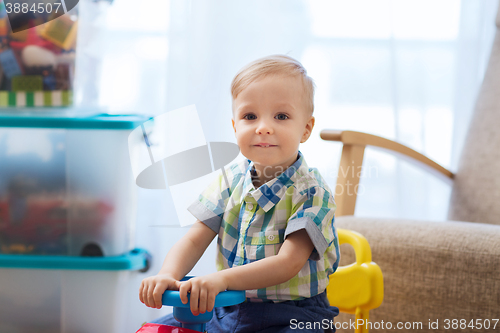 Image of happy little baby boy driving ride-on car at home