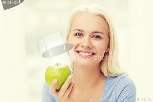 Image of happy woman eating green apple at home