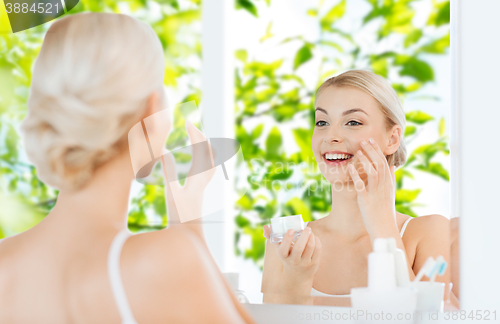 Image of happy woman applying cream to face at bathroom