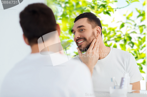 Image of happy young man looking to mirror at home bathroom