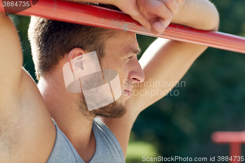 Image of young man exercising on horizontal bar outdoors