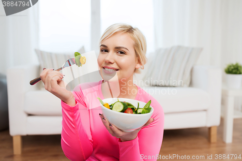 Image of smiling young woman eating salad at home