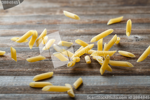 Image of Falling penne pasta. Flying yellow raw macaroni over black background.