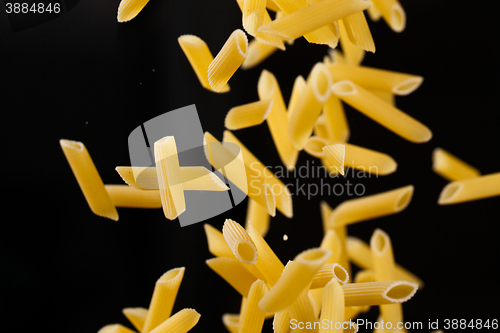 Image of Falling penne pasta. Flying yellow raw macaroni over black background.