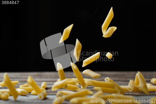 Image of Falling penne pasta. Flying yellow raw macaroni over black background.