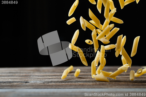 Image of Falling penne pasta. Flying yellow raw macaroni over black background.