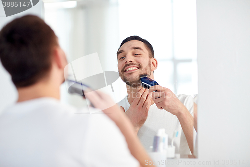 Image of man shaving beard with trimmer at bathroom