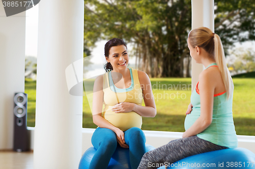 Image of two happy pregnant women sitting on balls in gym