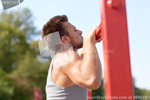 Image of young man exercising on horizontal bar outdoors