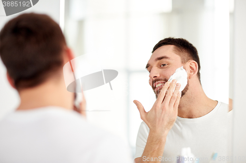 Image of happy man applying shaving foam at bathroom mirror