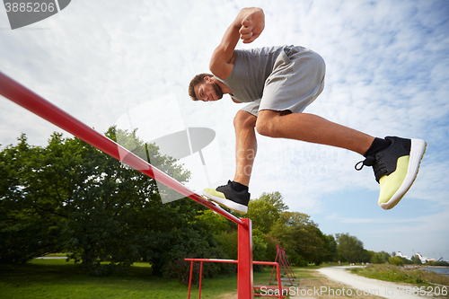 Image of young man jumping on horizontal bar outdoors