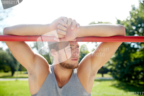 Image of young man exercising on horizontal bar outdoors