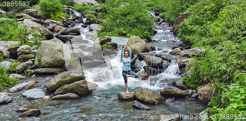 Image of Woman dpoing yoga asana tree pose at waterfall