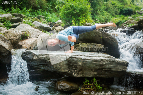 Image of Young fit woman doing yoga oudoors at waterfall