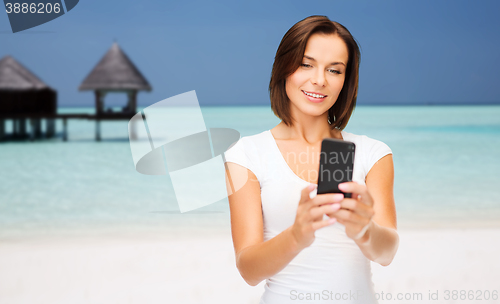 Image of happy woman taking selfie by smartphone over beach