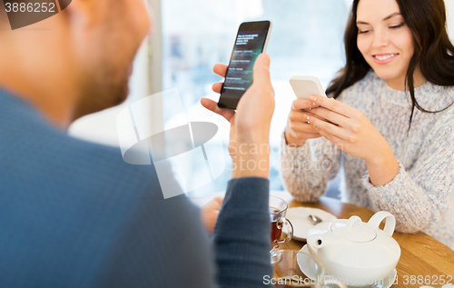 Image of happy couple with smartphones drinking tea at cafe