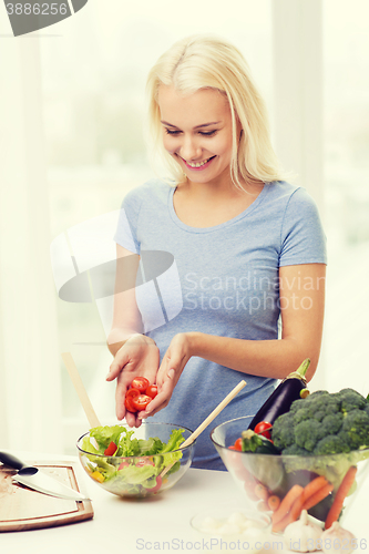 Image of smiling woman cooking vegetable salad at home