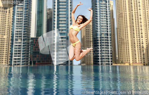 Image of happy young woman jumping over dubai city pool