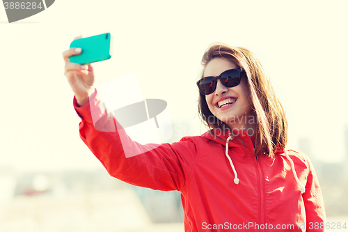 Image of smiling young woman taking selfie with smartphone