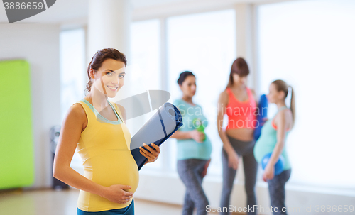 Image of happy pregnant woman with mat in gym
