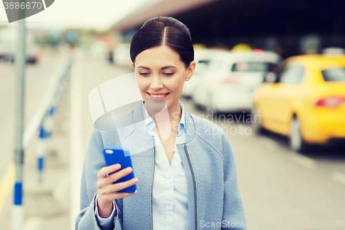 Image of smiling woman with smartphone over taxi in city