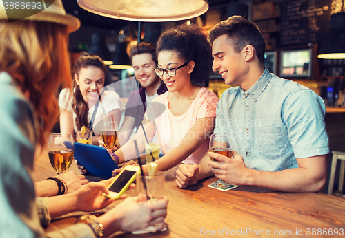 Image of happy friends with tablet pc and drinks at bar